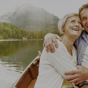 Smiling couple embracing in a boat on a lake with mountains in the background