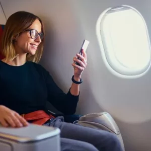 Woman with glasses smiling at her phone sitting in an airplane seat