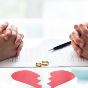 Two people with clasped hands across a table with a hear that has been broken in-between them.